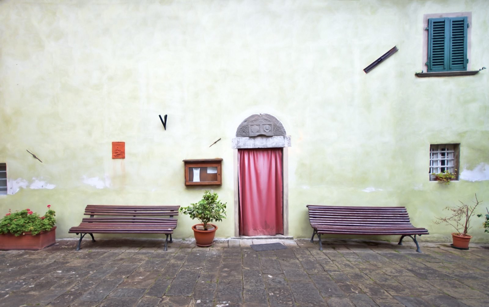 Two wooden benches either side of a pink door on a pale green wall in Aramo