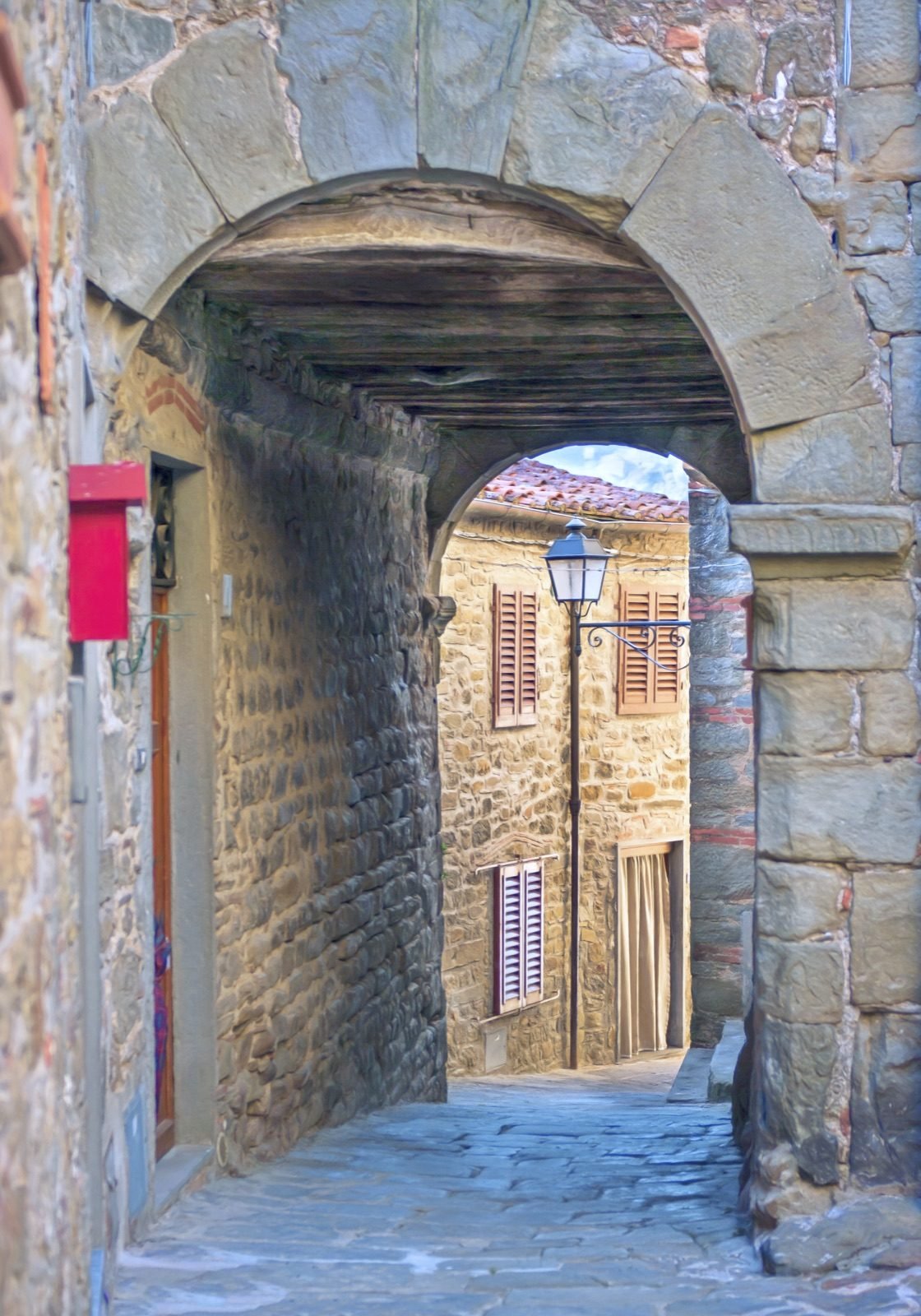 A covered stone passage under a round arch in Aramo, leading through to a sunny lane