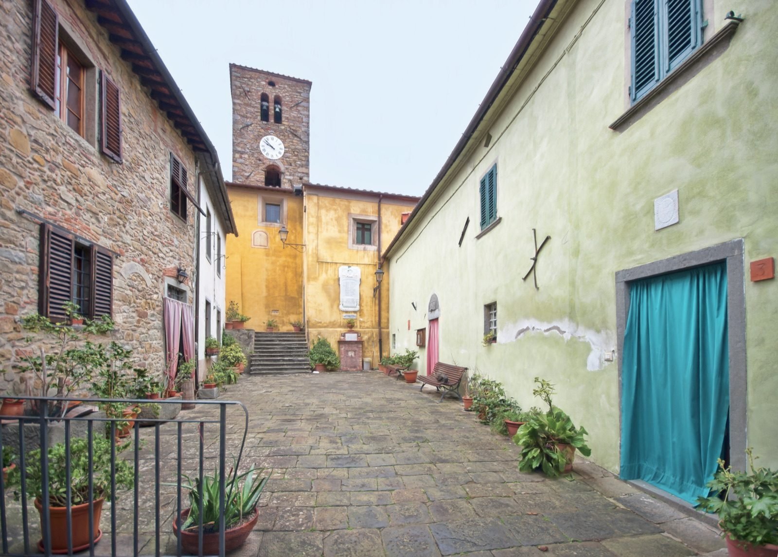 The little paved piazza of Aramo with pot plants, a blue door and the bell tower at the end