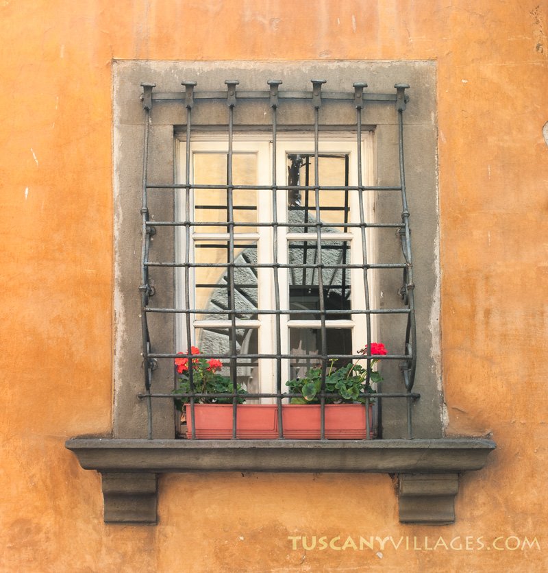 A barred window with flower boxes in an ochre wall in Bagni di Lucca