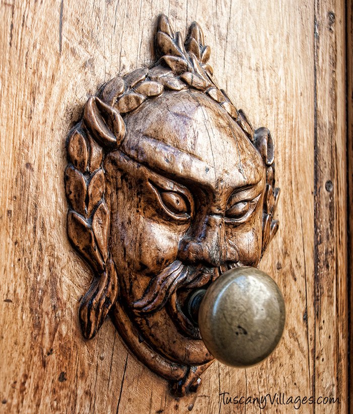 A carved bronze door knob in the shape of a face on an old wooden door in Barga