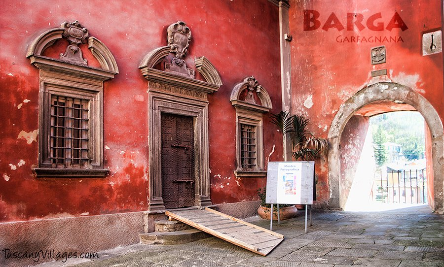 Carved stone windows and a doorway in a red-painted wall in Barga