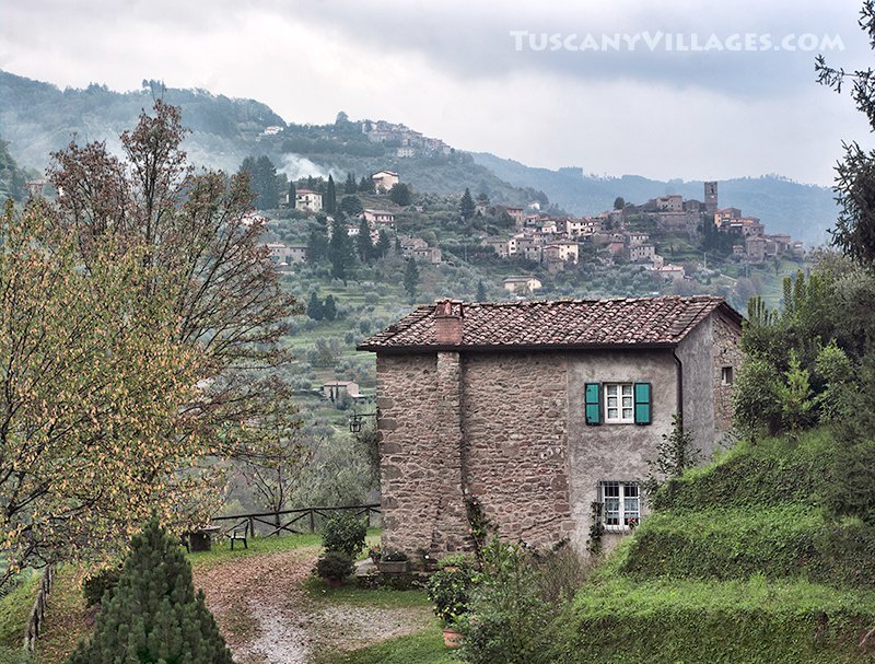 A stone farmhouse with the village of Castelvecchio on the hillside behind