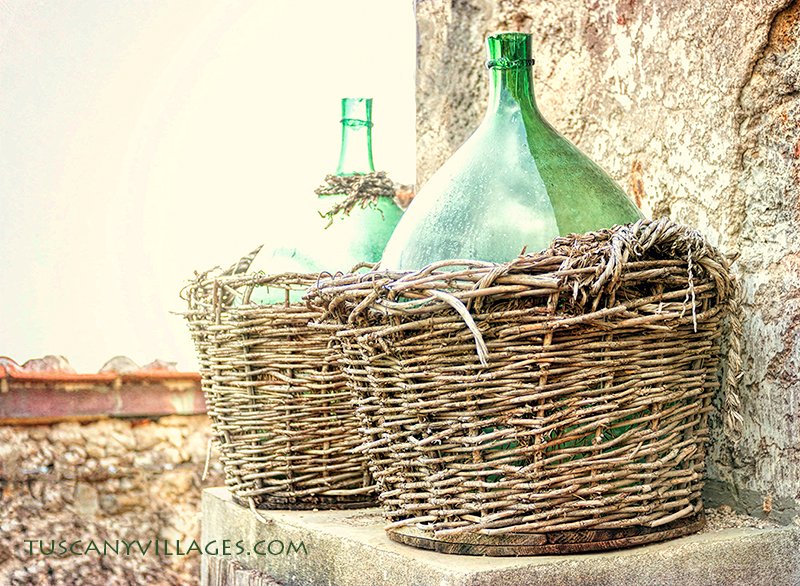 Two green glass demijohns in wicker baskets against an old stone wall