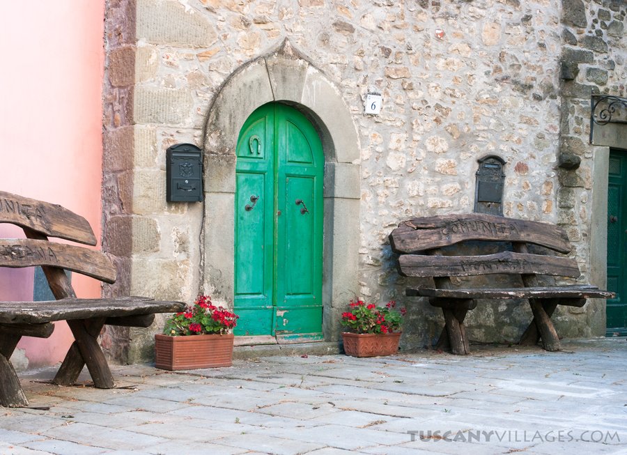 A green door with little seats outside a stone house in Fibbialla