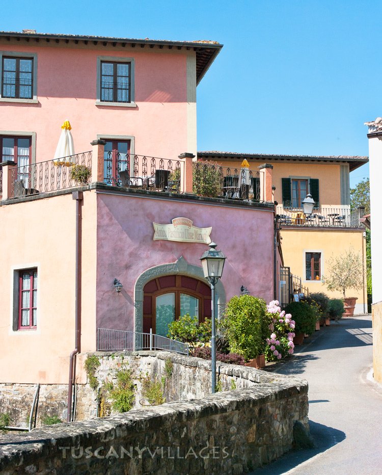 A pink house with green shutters and flowers on a sunny street in Greve in Chianti