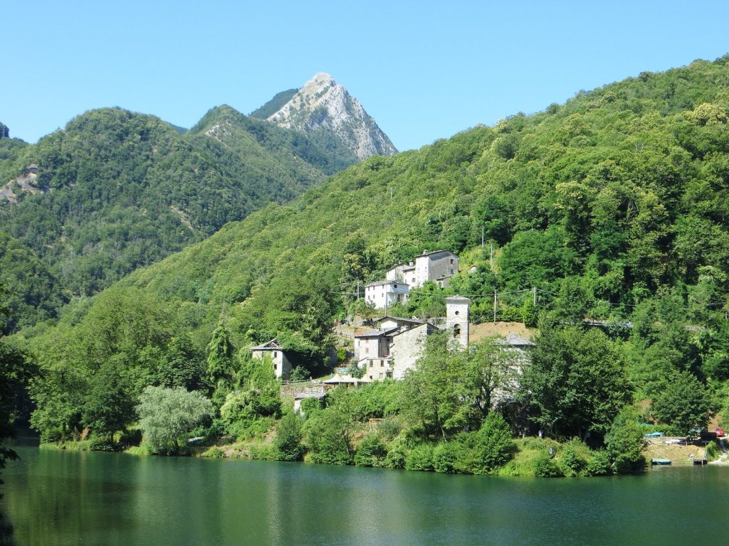 The stone hamlet of Isola Santa above a green lake, with wooded mountains behind