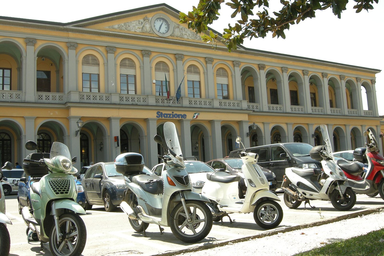 The pale front of Lucca railway station with scooters parked outside