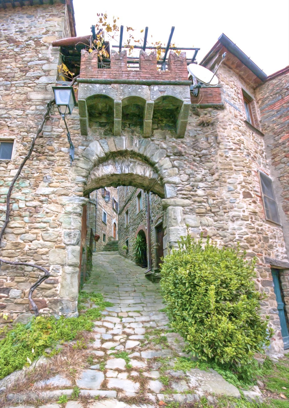 A stone archway leading into a narrow lane in Medicina