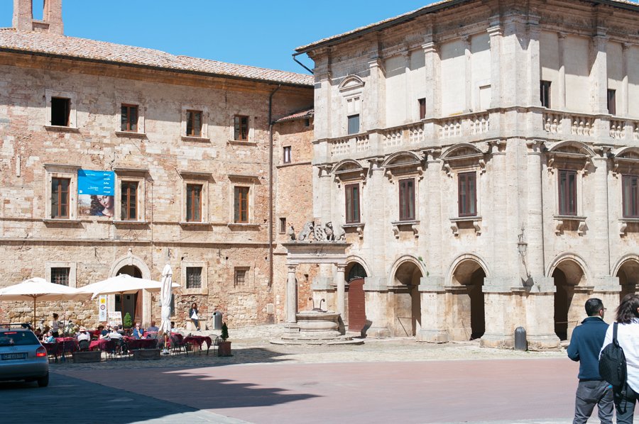 Stone palaces and an arcaded Renaissance palazzo around the Piazza Grande in Montepulciano, with café umbrellas