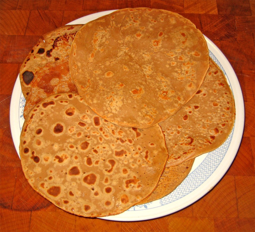 A stack of thin brown chestnut flour pancakes on a white plate