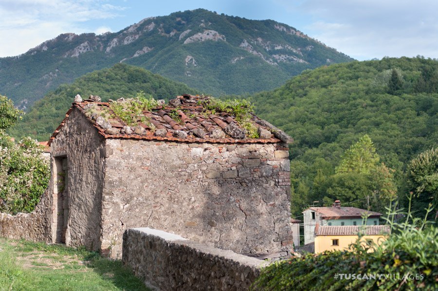 An old stone hut with a grassy roof in front of a wooded mountain near Casoli