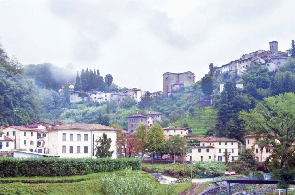 Pietrabuona and its tower on the wooded hillside, with low cloud over the hills