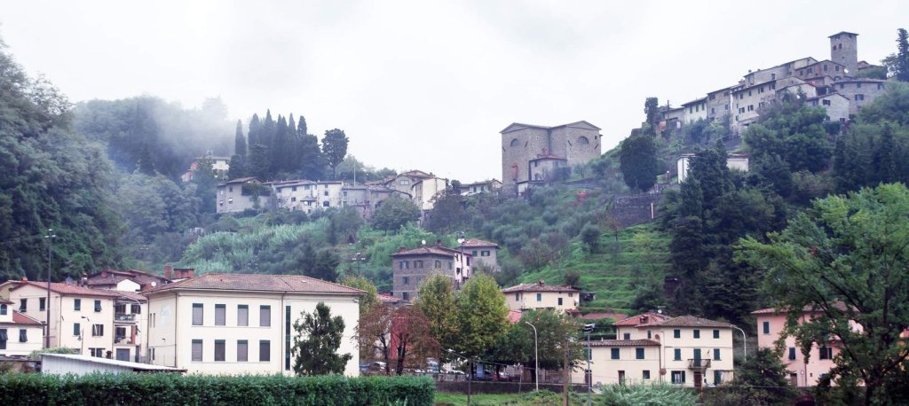 Pietrabuona and its tower on the wooded hillside, with mist hanging over the valley