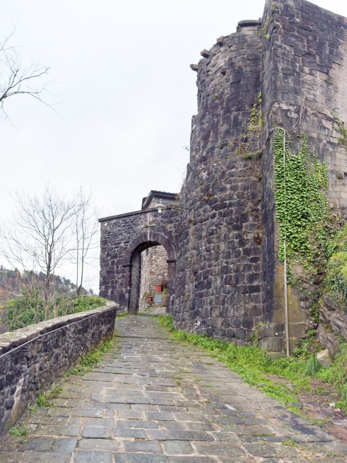 A stone-paved path climbing to an old gateway beside a ruined stone tower in Pietrabuona