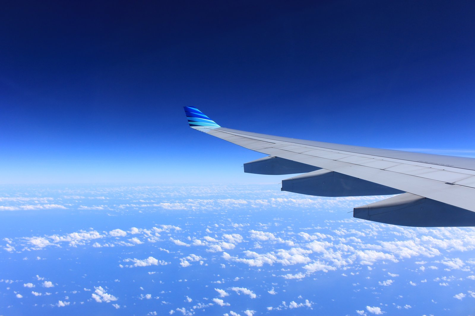 An aeroplane wing above white clouds and a deep blue sky
