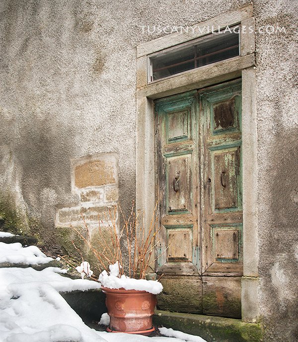 A green door in a stone house with snow on the step in Pontito