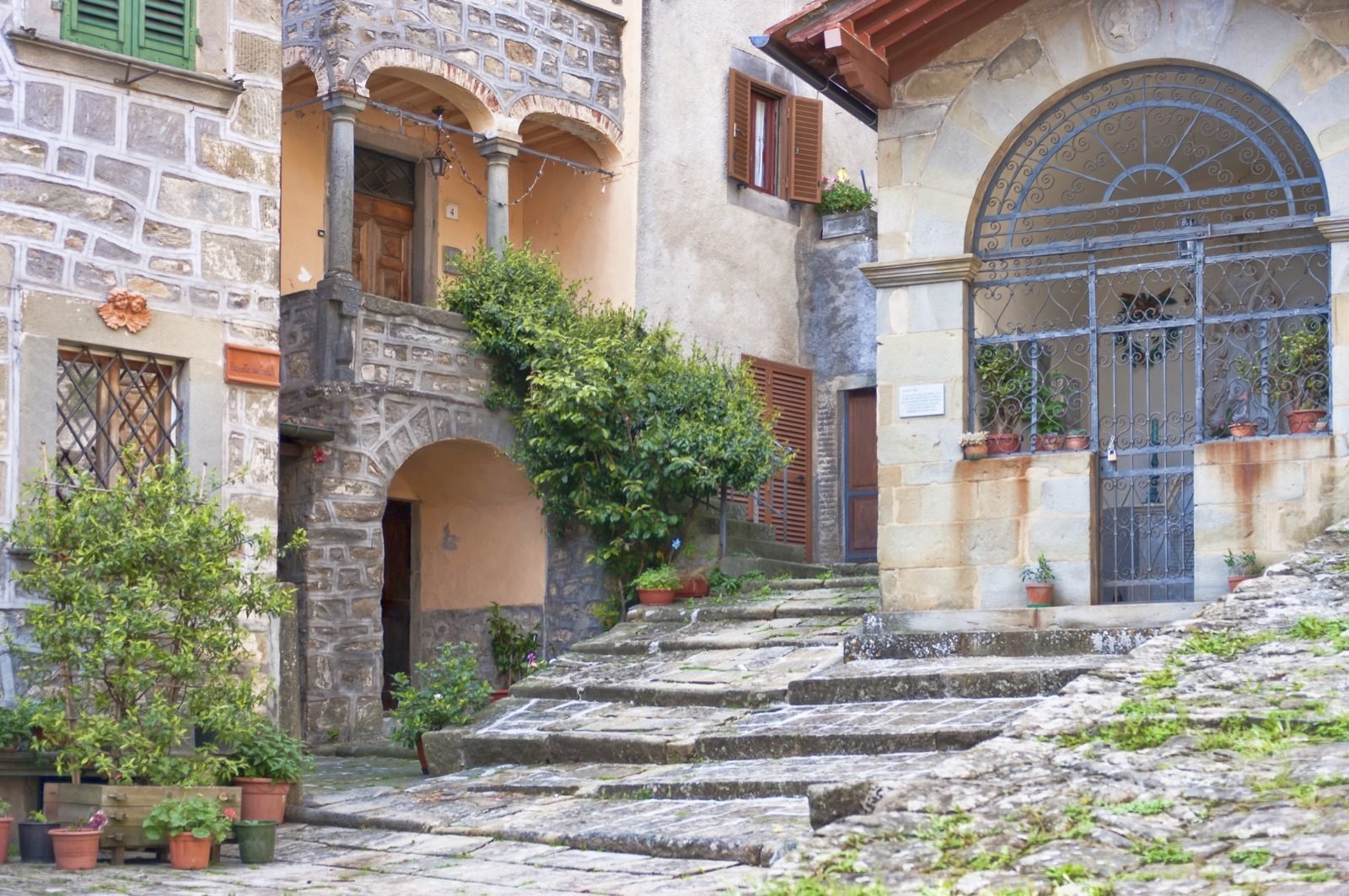 Worn stone steps and potted plants beneath arches and an arched gate in San Quirico