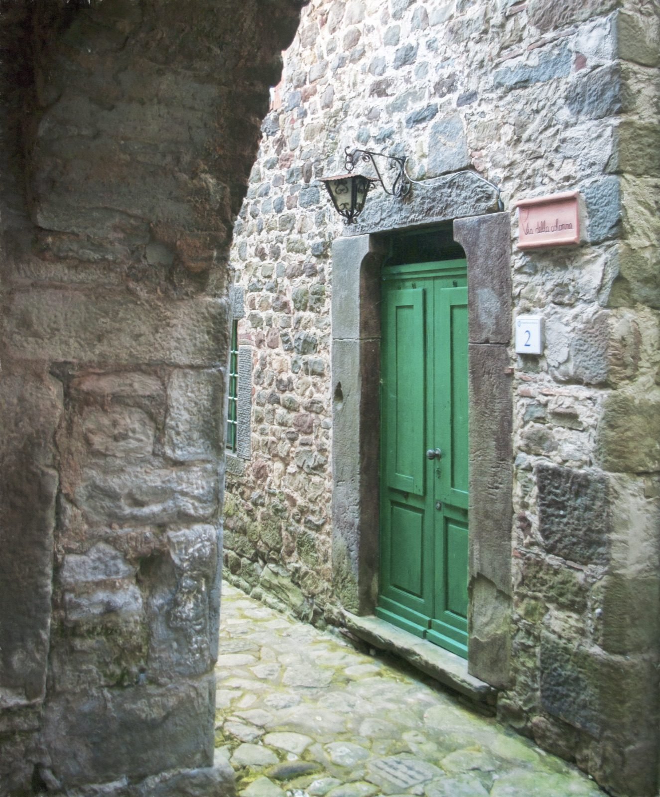 A green door in a stone wall seen through a dark archway in San Quirico