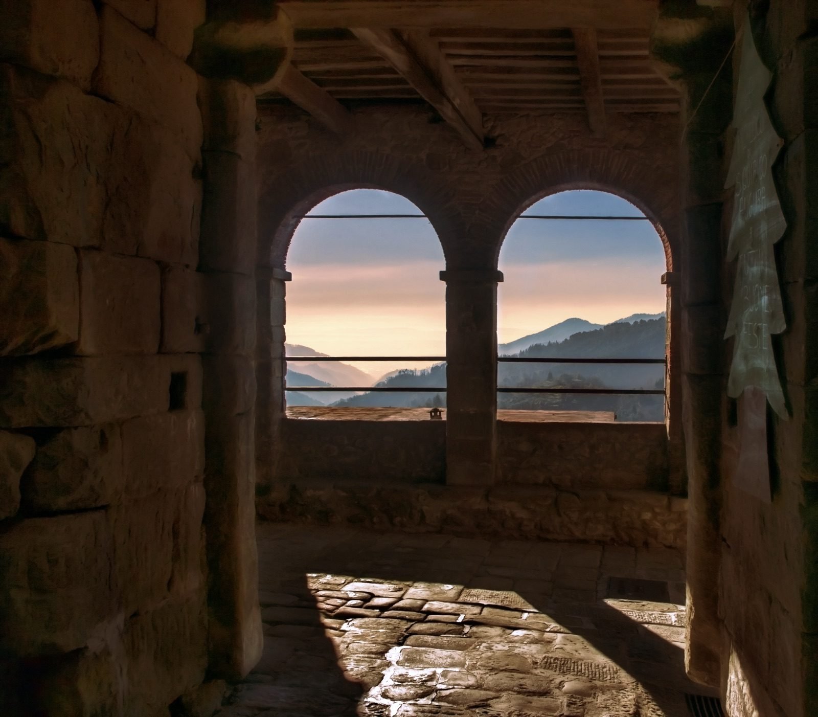 Two arched openings in a stone loggia in San Quirico looking out over the hills at sunset
