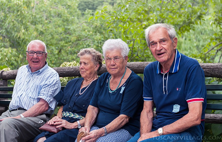 Two older couples sitting together on a bench in the piazza