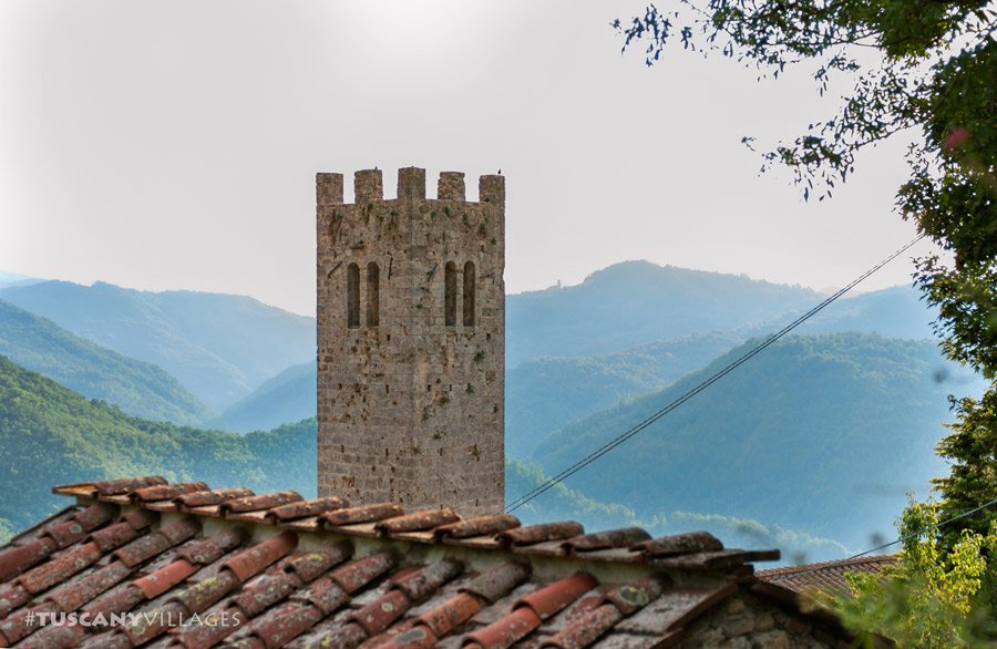 A medieval stone tower above terracotta roofs, with layers of blue hills behind
