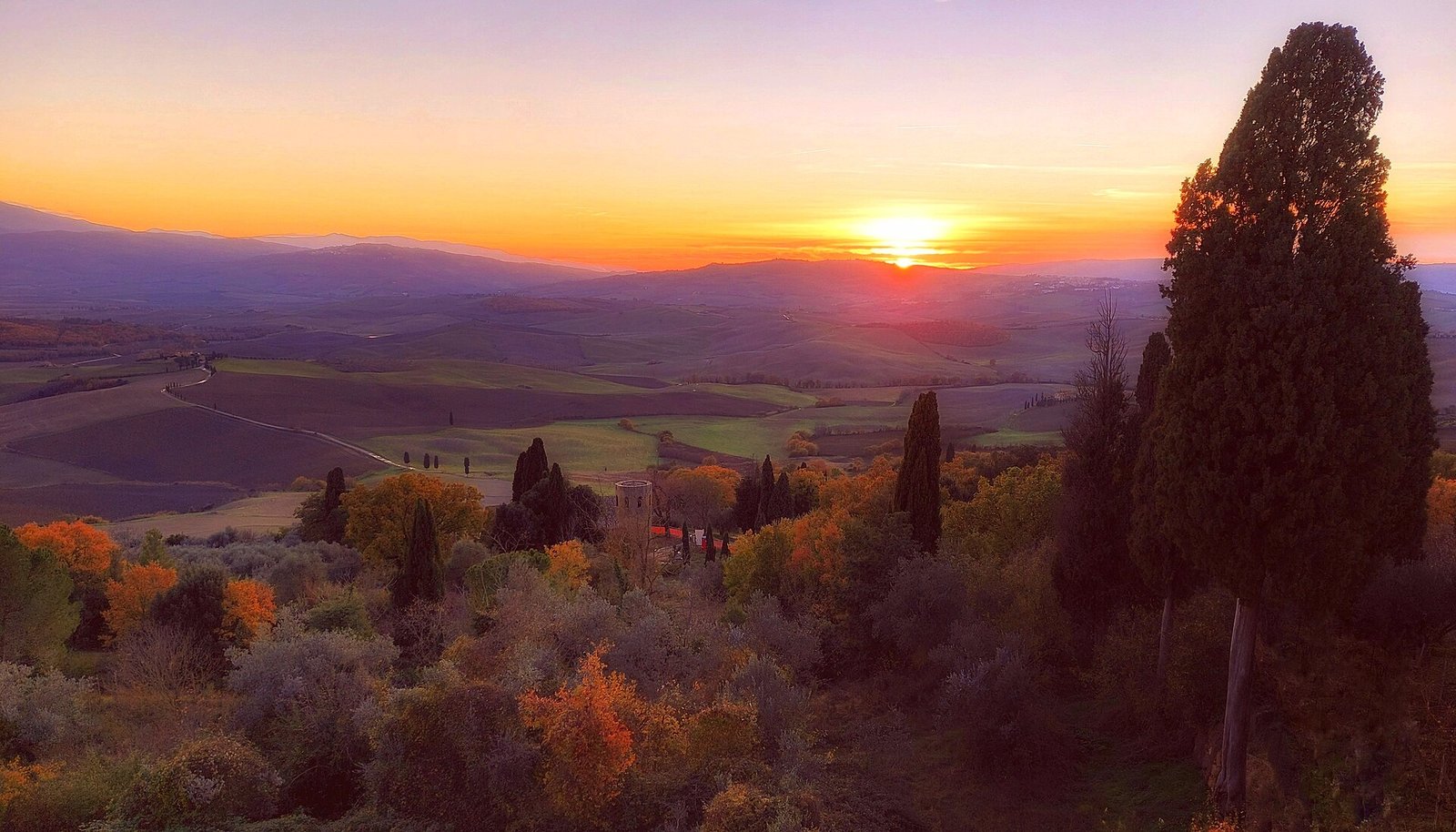 Sunset over the rolling hills and cypress trees of the Val d'Orcia, seen from Pienza