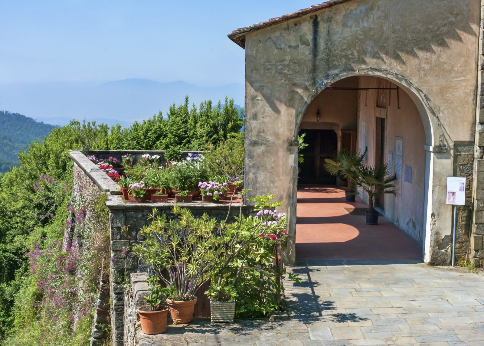 A stone archway opening onto a sunny terrace with a view in Vellano