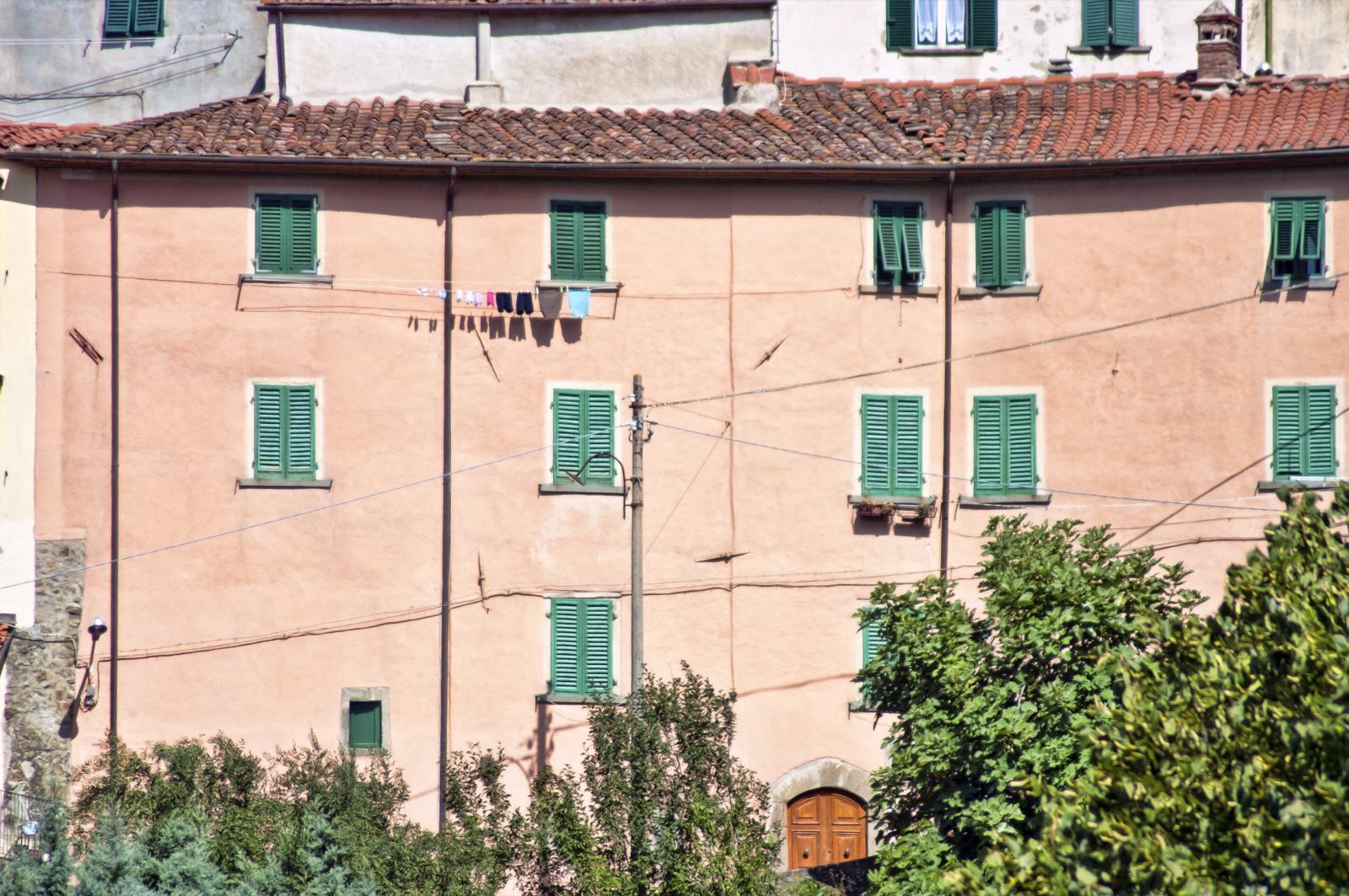 A tall pink village house with green shutters in Vellano
