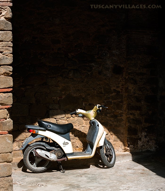 A white scooter parked in the shade of an old stone doorway
