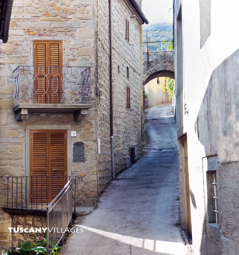 A shuttered stone house on a village lane leading to an arch